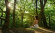 © USM Photography - Shot of one young women doing yoga in the green sunrise forest. Fitness people sitting on the exercise mat and relaxing in lotus yoga position. Female model meditating in lotus pose turning back
