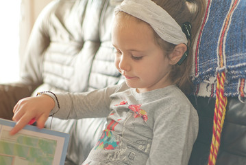 Blonde little girl with cochlear implant reading a book at home. Hear impairment and deaf community concept with empty copy space for Editor's text.