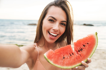 Wall Mural - Image of delighted woman eating watermelon and taking selfie photo