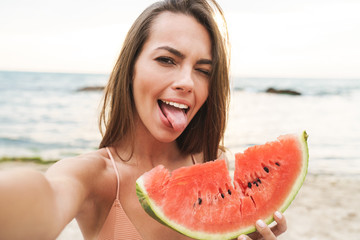 Wall Mural - Image of funny woman eating watermelon and taking selfie photo