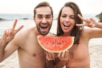 Wall Mural - Photo of couple holding piece of watermelon and gesturing peace sign
