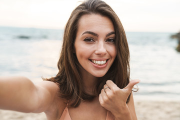 Poster - Image of smiling caucasian woman showing thumb up and taking selfie