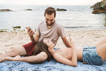 Poster - Photo of happy young couple using cellphones and smiling while lying