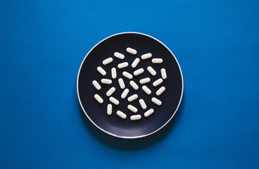 Wall Mural - Concept of human use of chemicals and dependence on them. White pills on plate on blue background. Dietary supplement Calcium Magnesium Zinc.   Flat lay.