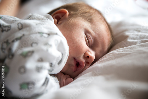 Cuadros en Lienzo adorable bebé durmiendo en la cama entre sábanas blancas