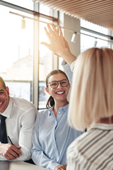 Two laughing young businesswomen high fiving together in an offi