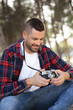Hombre joven y apuesto con cámara analógica tomando fotos en medio de la naturaleza.	