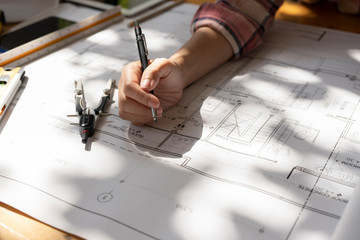  Top view, Woman Architect or engineer hands working on blueprint plans with a pencil ,laptop a ruler, calculator, and engineering tools. Architect or engineer working on blueprint in office.