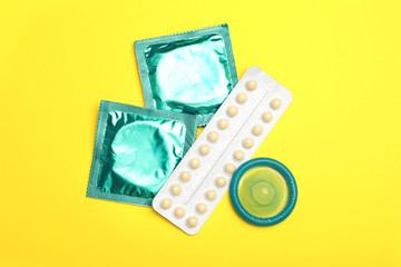 Wall Mural - Condoms and birth control pills on yellow background, flat lay. Safe sex concept