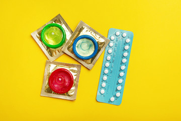 Wall Mural - Condoms and birth control pills on yellow background, flat lay. Safe sex concept