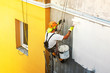 © predragmilos - Industrial rope access worker hanging from the building while painting the exterior facade wall. Industrial alpinism concept image. Top view