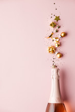 Flat Lay Of Celebration. Champagne Bottle And Golden Decoration On Pink Background