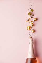 Flat lay of Celebration. Champagne bottle and golden decoration on pink background