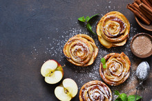 Dish of apple roses baked in puff pastry on a dark concrete background with apples. View from above