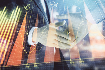 Double exposure of financial chart on cityscape background with two businessmen handshake. Concept of financial analysis and investment opportunities