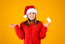 Close Up Portrait Of Young Beautiful Woman With Light Make Up On, Wearing Red Knitted Sweater & Santa Claus Hat. Attractive Female In Winter Knitwear Outfit, Isolated On Yellow Background. Copy Space