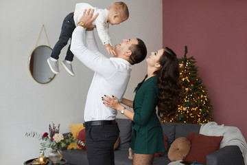 Wall Mural - Stylish happy couple and the cute little baby boy have fun at Christmas interior. Young parents with little son celebrating New year. Holidays of beautiful young woman, handsome man and their son.