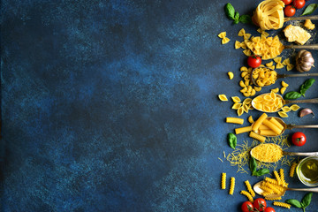  Assortment of pasta on a spoons with ingredients for making : tomato, parmesan chheese, garlic, basil and olive oil. Top view with copy space.