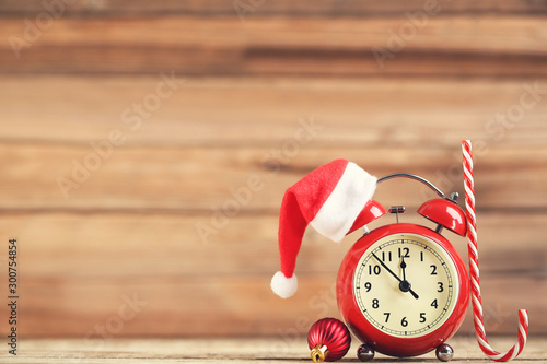 Fotomural Red alarm clock with santa hat, candy and bauble on brown wooden background