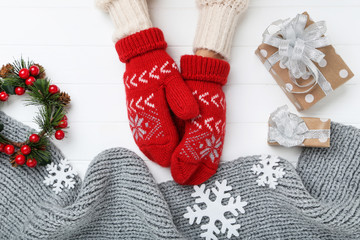 Poster - Hands in knitted mittens with grey scarf, snowflakes and gift boxes on white wooden table