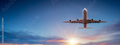 Fotomural Commercial airplane flying above dramatic clouds during sunset.