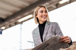 © Daniel Ingold/Westend61 - Smiling young businesswoman with newspaper at the train station