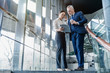 © InsideCreativeHouse - Two business partners holding documents and discussing business plans together while standing at business center stairs
