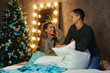 © Vagengeim - Lovely girl having fun while fighting pillows with his partner in comfortable home interior, romantic couple playing with pillows feeling carefree during winter Christmas holidays together.