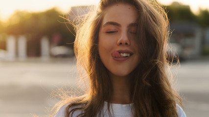 Back light portrait of a happy single teen girl breathing fresh air in a city street during a sunny day at sunset in a park with a warm yellow light and urban background. Summertime. Lifestyle.