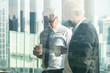 © Mongkolchon - business background of two businessman standing together with hands holding a cup of coffee during having business talking, view through office window