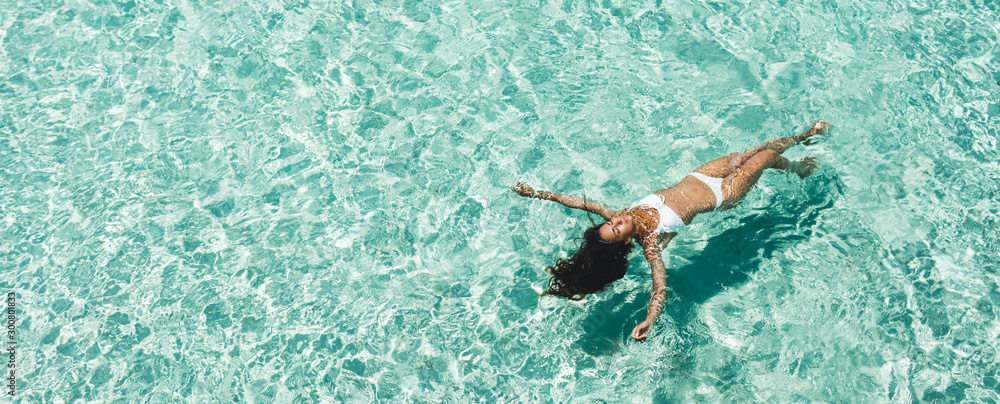 Woman in white bikini lying on transparent turquoise water surface on beach. Travel and vacations concept. Tropical background with empty space - obrazy, fototapety, plakaty 