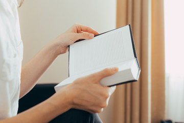 Beautiful female hands hold an open book or magazine in the room