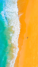 Aerial View Of The Beach With Waves On The Shoreline And Surfer Walking Along The Beach
