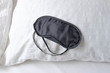 Eye mask on bed in room. Black headband for sleeping on a white pillow. Top view