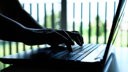 silhouette hands of programmer / computer hacker typing coding keys on laptop keyboard, attack signi