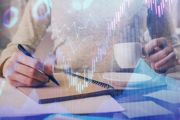 Forex chart hologram on hand taking notes background. Concept of analysis. Double exposure