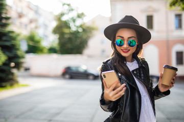 Young pretty asian woman holding phone and coffee cup walking on the city street