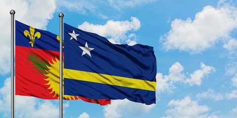 Guadeloupe and Curacao flag waving in the wind against white cloudy blue sky together. Diplomacy concept, international relations.