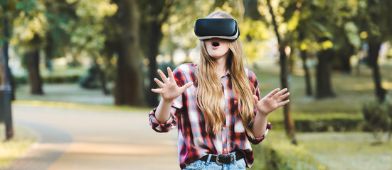 Wall Mural - panoramic shot of surprised young girl in casual clothes using vr headset