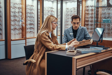 Poster - Professional salesperson helps a woman to choose reading glasses in an optometric shop.