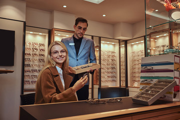 Sticker - Male oculist is helping female to choose pair of eyeglasses in ophthalmic shop.