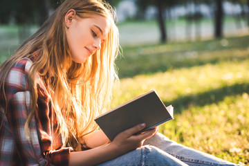 Wall Mural - side view of beautiful girl in casual clothes sitting on meadow in sunlight and reading book