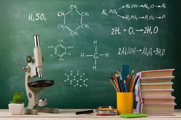 Education and science concept - group of colorful books and microscope on the wooden table in the classroom