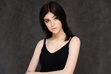 Close-up portrait of a young pretty girl student with long black hair, on a gray background. He stands right in front of the camera, showing his hands in different poses with different emotions.