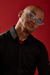 Wall Mural - Close-up shot of a man with shaved head in a black shirt over a red collar and with cat eyes retro sunglasses with a transparent half-frame and grayish lens. The photo is made on the red background.