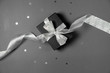 © Yura Yarema - Gift box wrapped in black paper with silver ribbon, stars confetti and price tags on gray background. Copy space and top view. Black friday box gift present isolated.