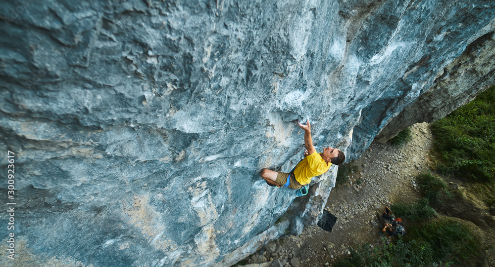 top view of man rock climber in yellow t-shirt, climbing on a cliff, searching, reaching and gripping hold. Conquering, overcoming and active lifestyle concept. - obrazy, fototapety, plakaty 