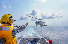 Signal Man Give Signal Hand To A Military Navy Helicopter Above Aviation Deck On The Ocean.  