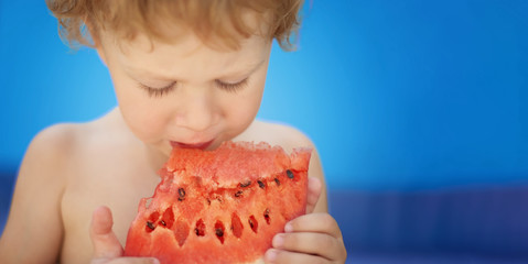 Boy eating slice of watermelon isolated on blue background. Free space to insert text