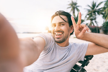 Wall Mural - Young male hipster traveler doing selfie overlooking on tropical beach. Adventure, vacation, wonderlust, internet, technology concept